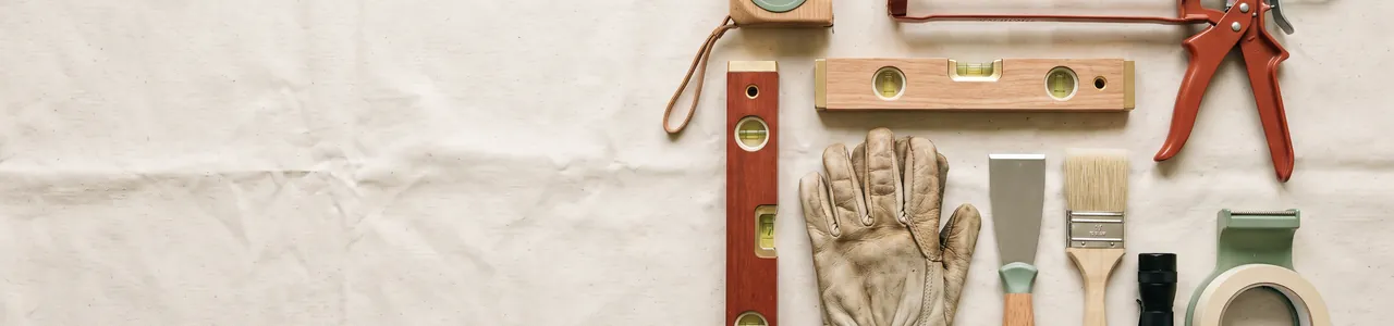 Basic home repair tools laid out on a canvas drop cloth: tape measure, levels, caulk gun, gloves, putty knife, brush, flashlight and tape